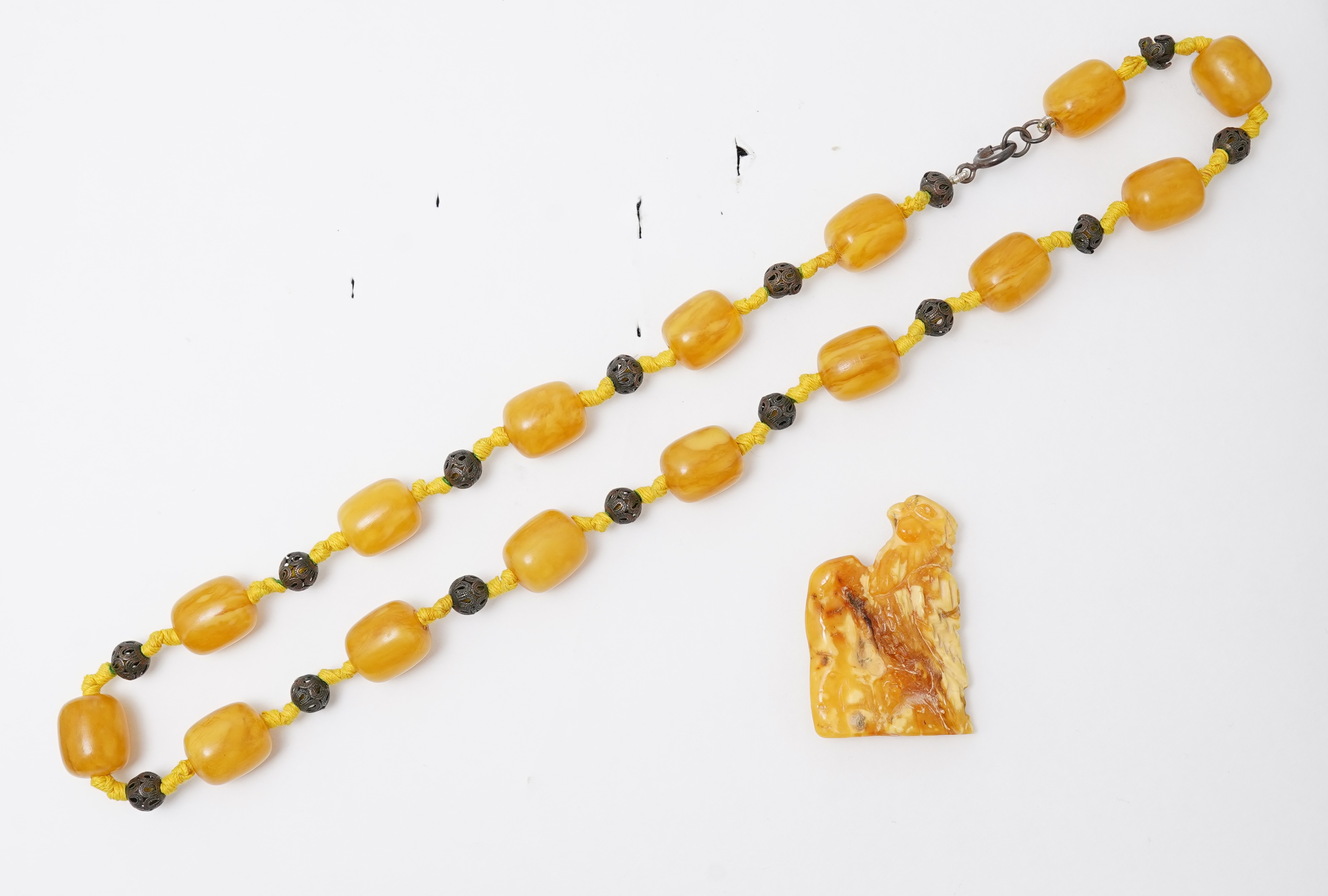 An amber necklace and carving, comprising: an amber necklace, composed of beads each measuring approximately 12 x 12 x 14mm, spaced by openwork metal beads, length 48cm; and an amber carving of a hawk on a rock, length 4